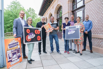 Preisträger des landesweiten Wettbewerbs „Jetzt brandheiß tauschen!“ halten symbolisch ihre hocheffizienten Neugeräte mit Energieeinsparung in die Kamera